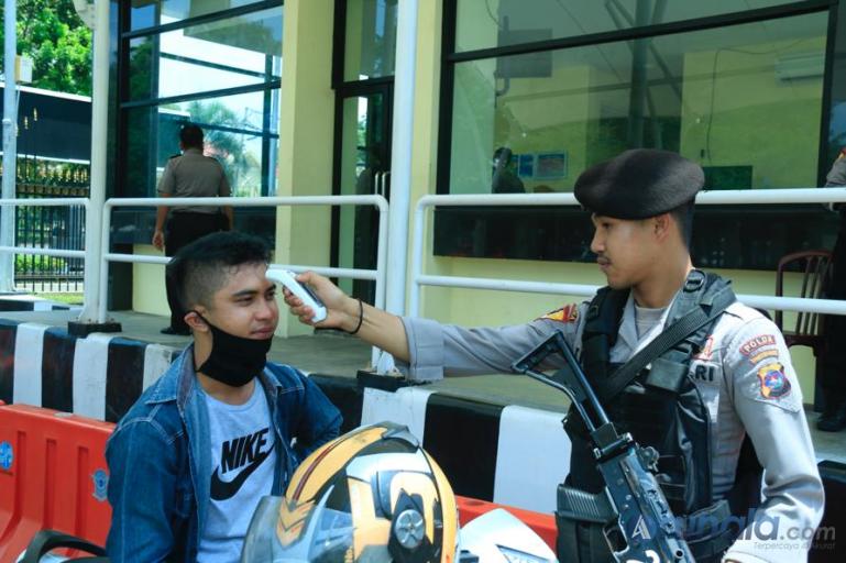 Seorang petugas memeriksa suhu tubuh pengunjung yang datang ke Mapolda Sumbar, Selasa (17/3). (Foto : Dyz)