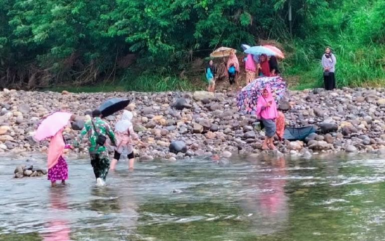 Babinsa Koramil 06/Koto Tangah, Serda Sunarto, bantu warga menyeberangi sungai di Batipuh Panjang, Kecamatan Koto Tangah, Kota Padang, beberapa waktu lalu. (Dok : Istimewa)