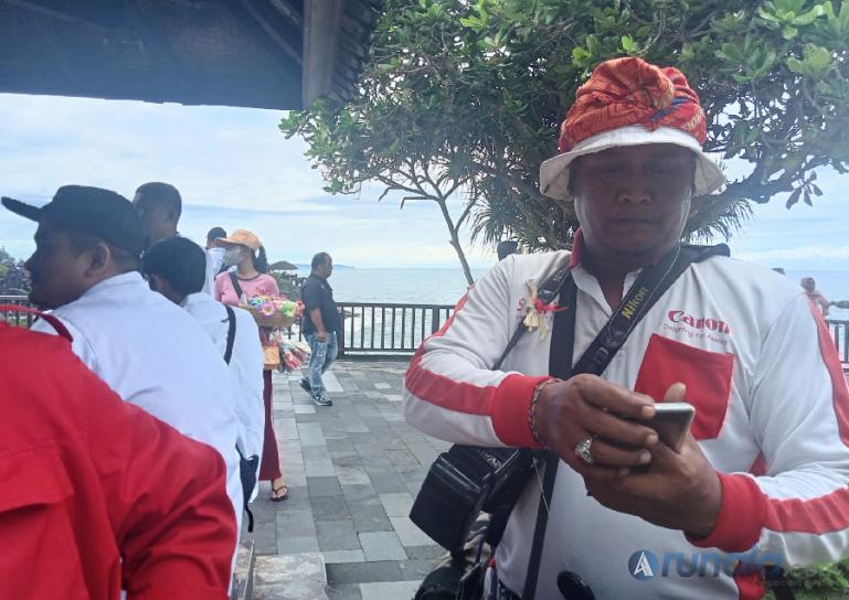 Ari, salah seorang juru foto keliling di tempat wisata Tanah Lot Bali sedang melayani para wisatawan yang berkunjung ke tempat wisata tersebut, Kamis siang (24/11). (Foto : Arzil)