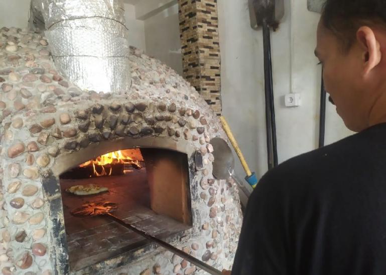 Proses pemanggangan pizza kayu bakar menggunakan tungku dari batu di dalamnya ada kayu bakar. (Dok : Istimewa)