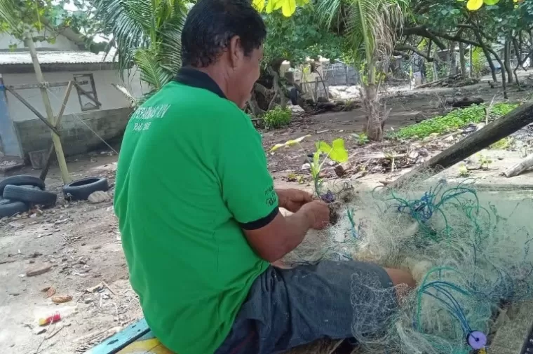 Afrizal sedang memperbaiki jaring nelayannya saat kondisi tingginya gelombang air laut yang merendam rumah warga di Kelurahan Air Tawar Barat, Rabu (16/10/2024). (dok : arunala.com)
